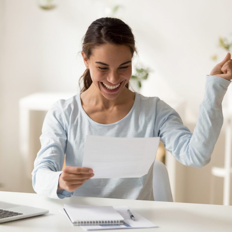 Overjoyed millennial mixed race female worker employee reading letter with good news, celebrating special achievement. Smiling young woman getting bank loan approval or lottery win notification.